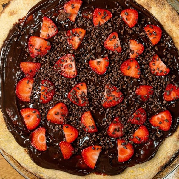 Dessert pizza with melted chocolate, fresh strawberry slices, and chocolate sprinkles on a golden crust.