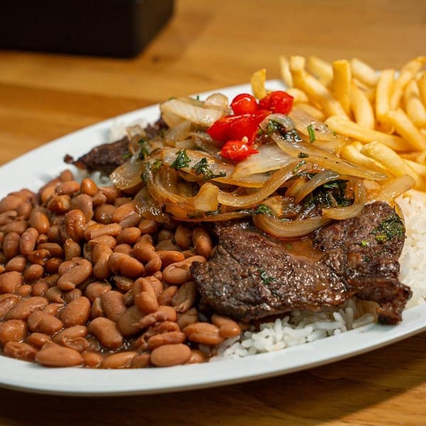 A plate of steak topped with onions and peppers, served with rice, beans, and french fries.