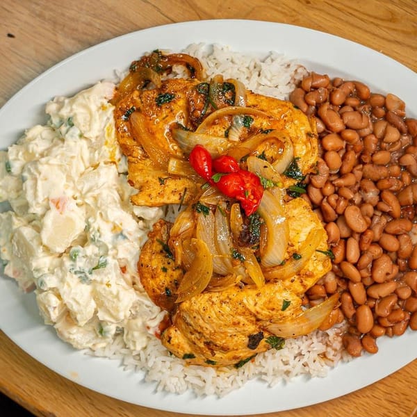 Chicken breast with onions, rice, beans, and potato salad on a white plate.
