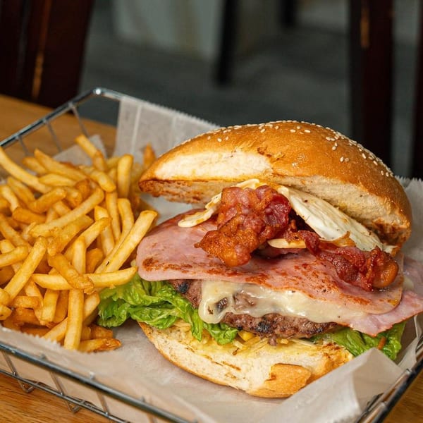 A gourmet burger with bacon, ham, cheese, and lettuce, served with a side of golden french fries.