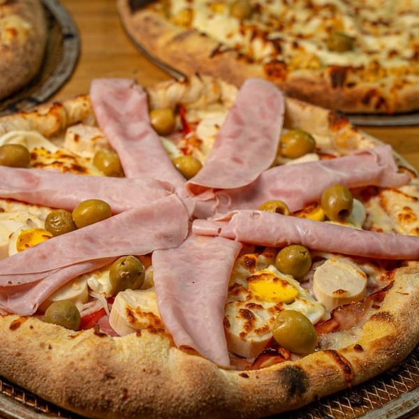 Close-up of a pizza topped with ham, olives, and fried eggs, with another pizza in the background.